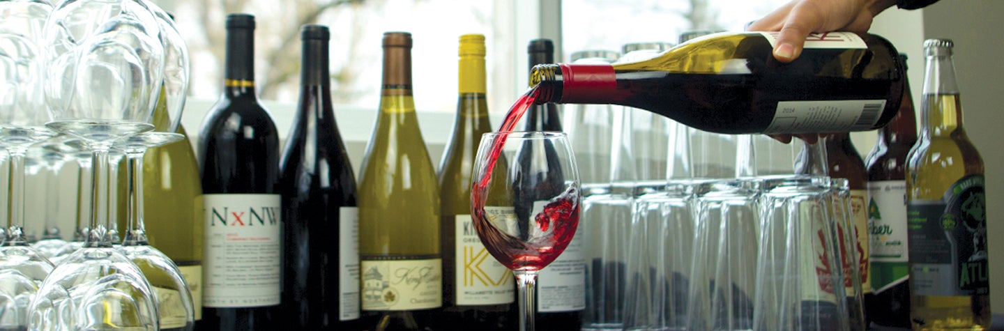 Catering staff pouring red wine into wine glass.